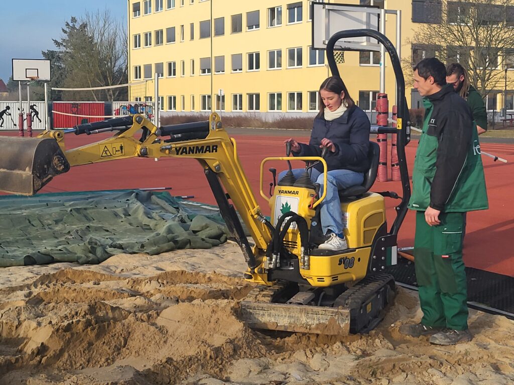 Eine Schülerin auf einem Bagger neben einem Mitarbeiter der Firma