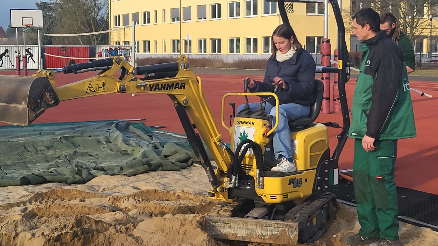 Eine Schülerin auf einem Bagger neben einem Mitarbeiter der Firma